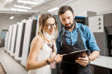 Young woman designer and print operator working together at the print manufacturing with offset...