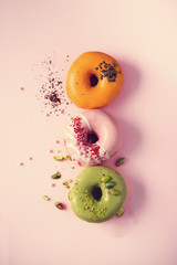Colorful donuts with icing on pastel pink background. Sweet orange, green, pink doughnuts with pistachio, chocolate. Flat lay, top view, copy space