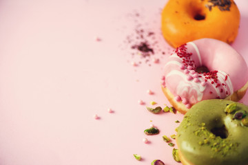 Colorful donuts with icing on pastel pink background. Sweet orange, green, pink doughnuts with pistachio, chocolate. Flat lay, top view, copy space