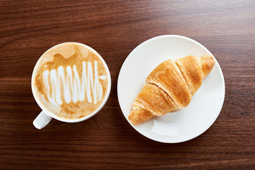Croissant with coffee cappuccino for breakfast. Top view isolated on wooden background.