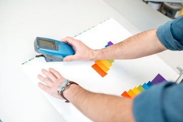 Measuring color on the paper print with spectrometer tool at the operating desk of the printing plant