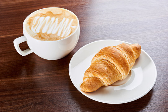 Croissant with coffee cappuccino for breakfast. Above view isolated on wooden background.