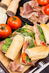 Fototapeta na wymiar Three healthy and delicious sandwiches on wooden board next to tomatoes, greenery, ham and cheese