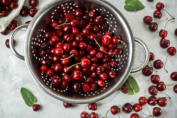 Top view at the colander with ripe cherries. Colander stands on a white surface.