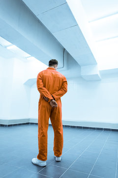 rear view of prisoner in orange uniform standing in prison cell