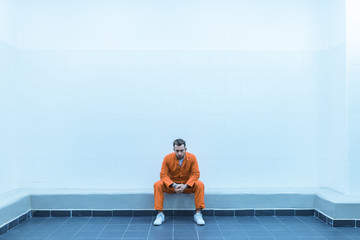 prisoner sitting on bench in prison room - obrazy, fototapety, plakaty