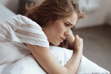Fototapeta premium What should I do. Worried woman lying on a bed and looking into vacancy while thinking about something serious.