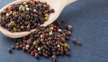 Top view on composition of peppercorns in wooden spoon on dark background, close-up.