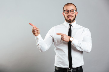 Photo closeup of content office worker in white shirt and eyeglasses smiling on camera and pointing fingers aside on copy space, isolated over gray background