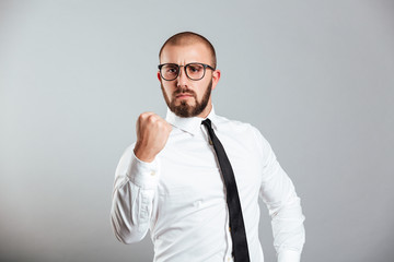 Photo of purposeful businessman in white shirt and eyeglasses gesturing fist on camera meaning fortitude, isolated over gray background
