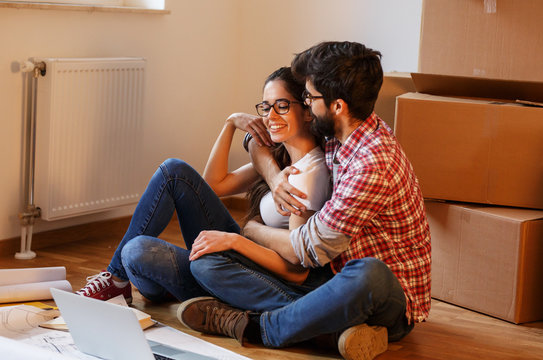 Young couple moving into a new house.They sitting on floor and calculate savings and home budget.Man embracing his wife.