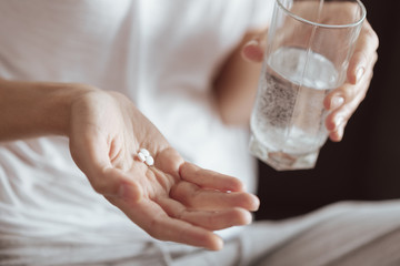 Struggling with pain. Scaled up look on a lady holding a glass of water and a several pills on her palm indoors.