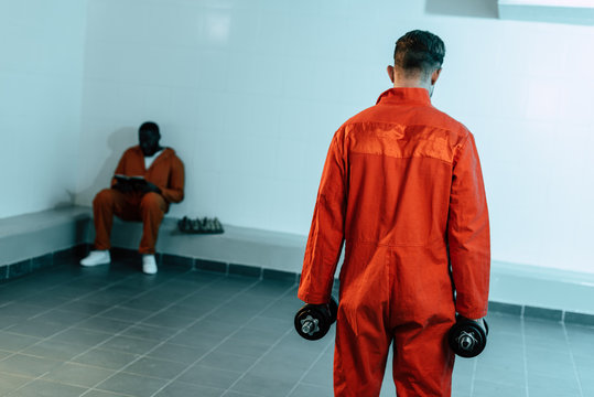 rear view of prisoner training with dumbbells in prison cell