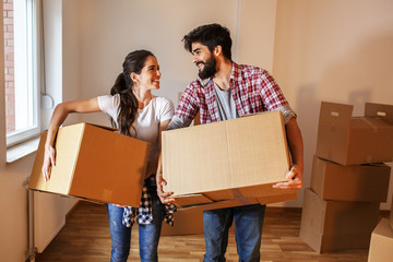 Young couple carrying big cardboard full of home essentials  into a new home.Moving house.Real estate concept. - obrazy, fototapety, plakaty