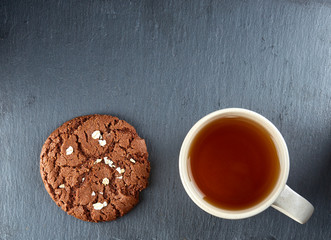 Close-up white cup of tea with chocolate cookies on dark background, top view