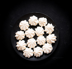 Sweet white meringue on a black wooden background, free space for text.