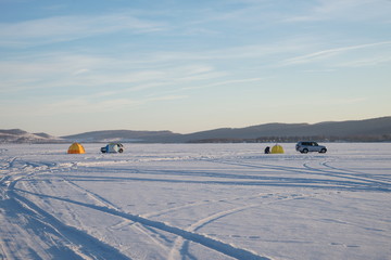 Winter  lake with tents and cars of fishermens against the background of mountains.