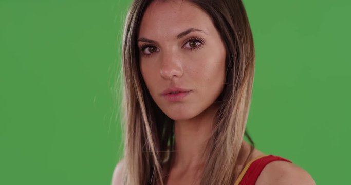 Close up portrait of millennial hipster woman in red top looking at camera with wind blowing her hair on greenscreen. Beautiful Caucasian girl in her 20s with long brown hair. 4k on green