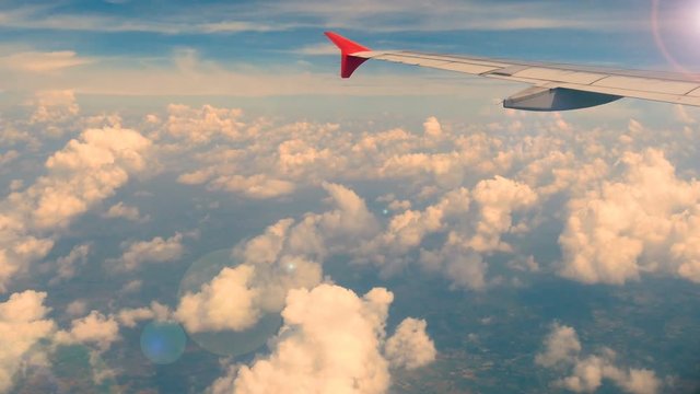 4K footage. traveling by air. aerial view through an airplane window. wing airplane at sunset or sunrise time with lens flare and beautiful white clouds in blue sky for background