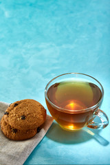 Glass cup of tea and chocolate cookies close-up on blue background.