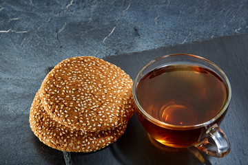 A glass cup of black tea with cookies on a dark greyish marble background. Breakfast background