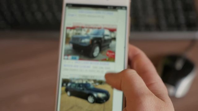 A man chooses to buy a car on the site. Looking at used vehicle to buy on a smartphone app. Close Up. Screen is blurred. 4K UHD.