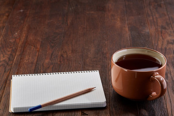 Cup of tea with cookies, workbook and a pencil on a wooden background, top view