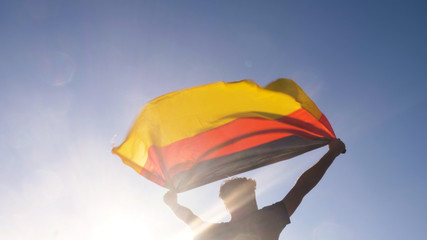Young man holding german national flag to the sky with two hands at the beach at sunset germany