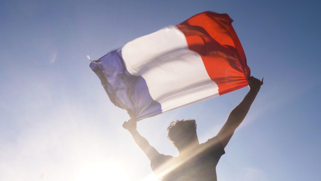 Young man holding french national flag to the sky with two hands at the beach at sunset france