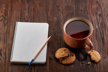 Cup of tea with cookies, workbook and a pencil on a wooden background, top view