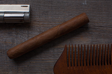 Comb for a beard, sigar, and lighter lies on a wooden background.