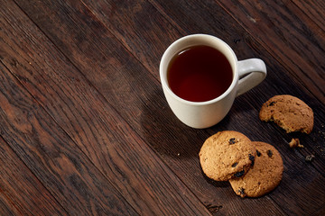 Cup of tea with cookies, workbook and a pencil on a wooden background, top view