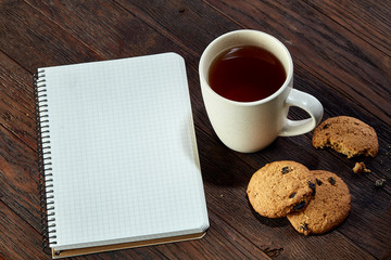 Cup of tea with cookies, workbook and a pencil on a wooden background, top view