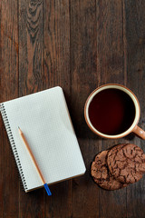 Cup of tea with cookies, workbook and a pencil on a wooden background, top view