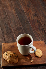 Cup of tea with cookies, workbook and a pencil on a wooden background, top view