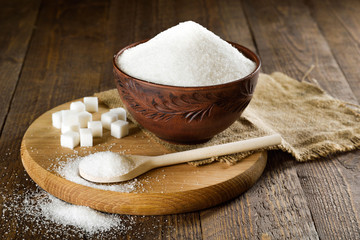 Bowl and spoon full of sugar on wooden background