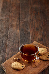 Cup of tea with cookies on a cutting board on a wooden background, top view