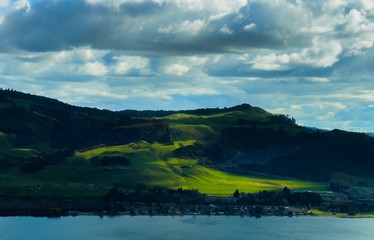 Obraz premium Amazing hill covered with greenery and exposed to sun rays from a small opening from the cloudy sky.