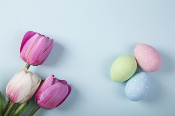 Easter Background with white and pink tulips and colorful quail eggs on blue stone table background