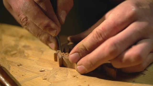 Closeup view of woodman working in craft studio, and carving patterns on small wooden material, with cutter slow motion