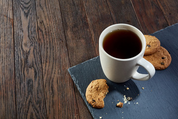 Cup of tea with cookies, workbook and a pencil on a wooden background, top view