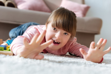 Happy child with down syndrome lying on floor in cozy room