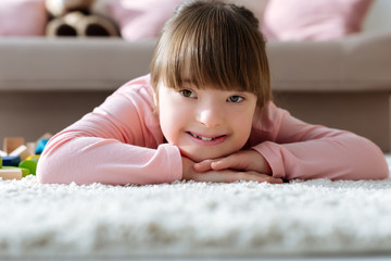 Smiling kid with down syndrome lying on floor