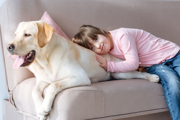 Kid with down syndrome lying on the sofa with Labrador retriever dog