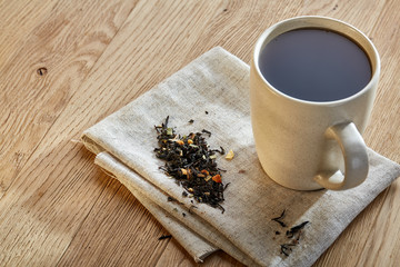 Ceramic cup of tea with scattered tea leaves on a napkin on rustic wooden background, selective focus