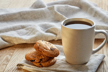 Porcelain teacup with chocolate chips cookies on cotton napkin on a rustic wooden background, top view