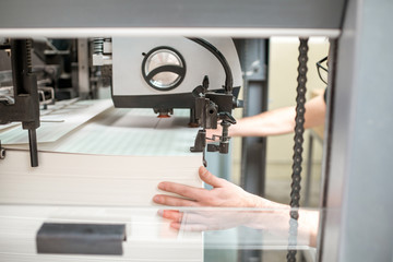 Worker filling up the paper sheets for printing into the offset printing machine at the...