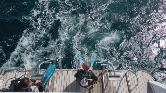 Slow motion An indistinguishable scuba diver sits on the edge of the boat. The boat is moving. View from above.
