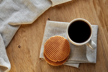 Obraz na płótnie Canvas Porcelain teacup with waffles on cotton napkin on a rustic wooden background, top view, vertical