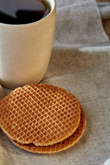 Porcelain teacup with waffles on cotton napkin on a rustic wooden background, top view, vertical